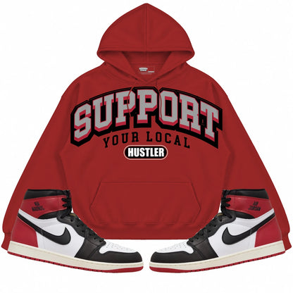 Rebranded Studios Support Your Local Hustler Air Jordan 1 High OG Black Toe Reimagined red hoodie — front with sneakers